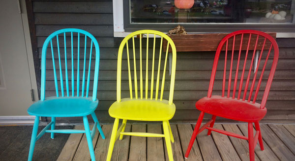 3 brightly colored wooden chairs on a porch