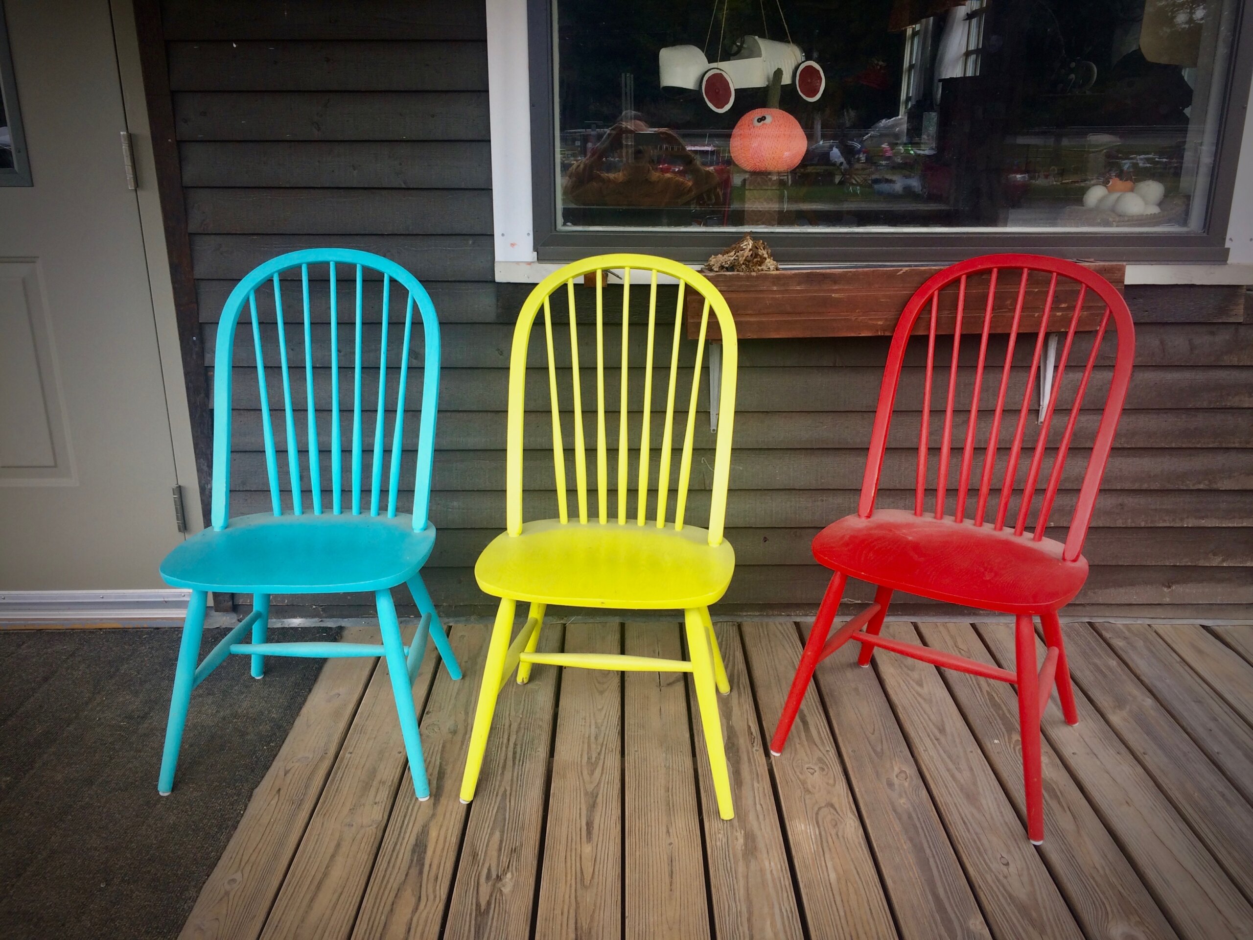 3 brightly colored wooden chairs on a porch