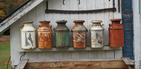 old metal jugs lined up outside a white barn
